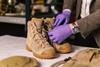 Brown, lace up boots being inspected on a table with someone in purple gloves.