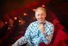 Alan Cumming sat in red theatre seat smiling at camera