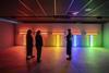 There are three people in a shadowed room, admiring light displays of many colours.