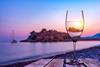 Wineglass on old wooden table on the beach of Sveti Stefan at sunset, Montenegro
