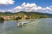 A long cruise ship sailing past a riverfront village
