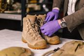 Brown, lace up boots being inspected on a table with someone in purple gloves.