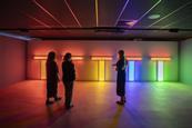 There are three people in a shadowed room, admiring light displays of many colours.