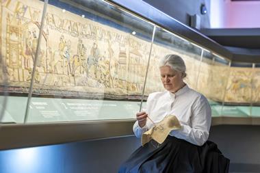 Woman doing embroidery while sat next to Britain's Bayeux Tapestry