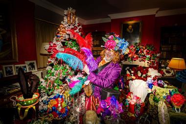 A man dressed as the Mad Hatter holding colourful feathers in front of a christmas tree