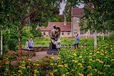 Three people looking at Henry Moore sculpture surrounded by gardens