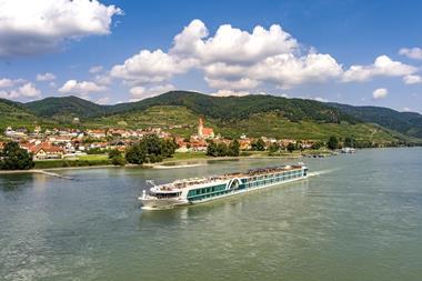 A long cruise ship sailing past a riverfront village