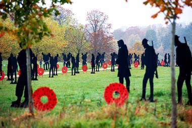 Several black silhouettes and poppy wreaths line a footpath through a park