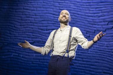 Man poses with arms out in front of blue brick wall