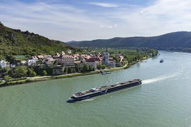 A long cruise ship sailing past a riverfront vilage