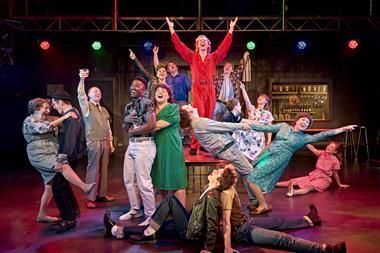 Group of characters on stage singing and dancing under coloured lights
