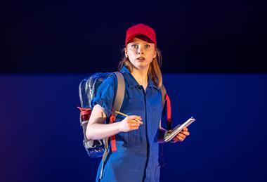 Young woman wearing red hat, blue boiler suit and holding note pad and pen