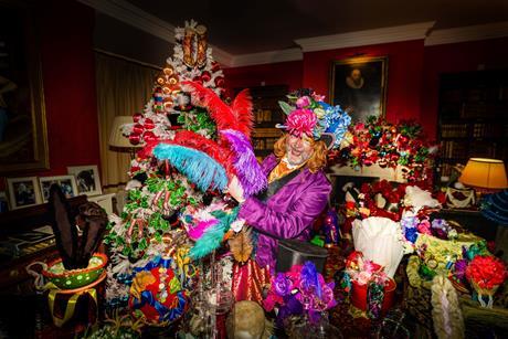 A man dressed as the Mad Hatter holding colourful feathers in front of a christmas tree