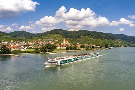 A long cruise ship sailing past a riverfront village