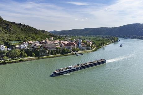 A long cruise ship sailing past a riverfront vilage