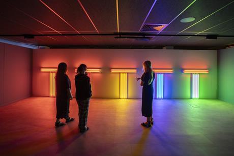 There are three people in a shadowed room, admiring light displays of many colours.