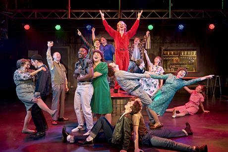 Group of characters on stage singing and dancing under coloured lights