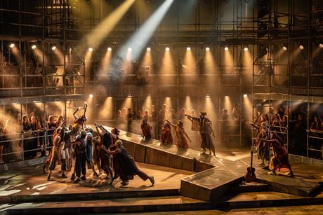 Cast members on stage performing around scaffolding building