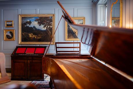 Inside Handel's residence on Brook Street, Mayfair showing one of the music rooms with a piano and various paintings on the wall.