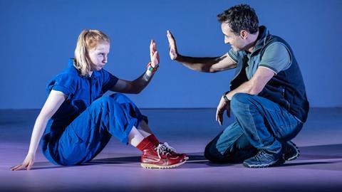 Man and young woman sat on the floor holding up their hands to each other