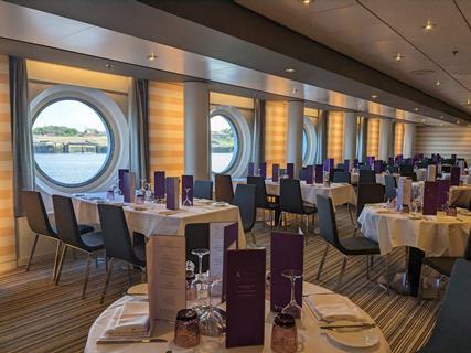 Inside Buckingham Restaurant on board Ambassador's Ambition ship, showing tables set for dinner.