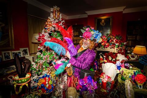 A man dressed as the Mad Hatter holding colourful feathers in front of a christmas tree