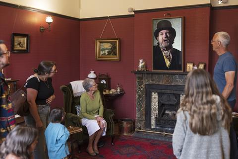 A group in a Victorian living room looking at a man's portrait