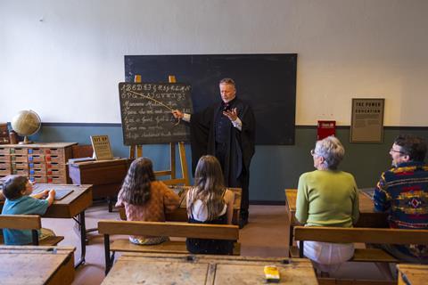 A mock Victorian classroom with teacher in front of groups of kids and adults