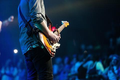 Man playing a guitar at a music concert with audience in the background
