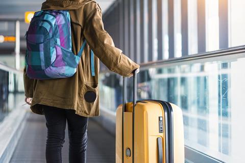 Girl riding on the travellator at the airport with a large yellow suitcase.