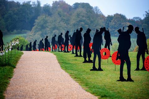 Several black silhouettes and poppy wreaths line a footpath through a park