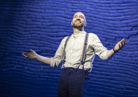Man poses with arms out in front of blue brick wall