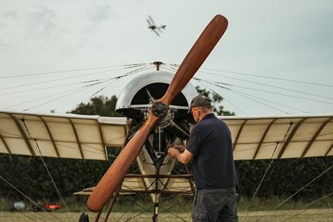 Man assisting with historic aeroplane on the ground with another plane flying above.