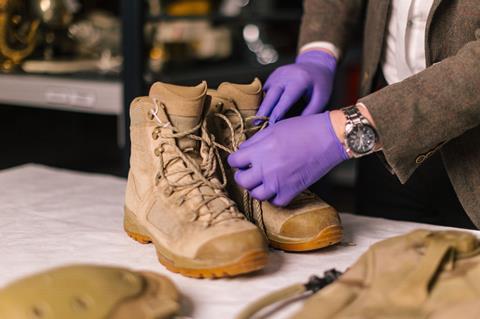 Brown, lace up boots being inspected on a table with someone in purple gloves.