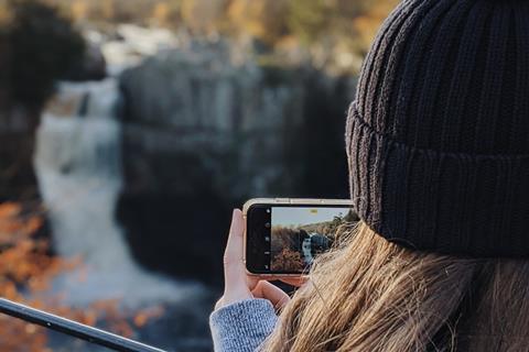 A woman taking a photo of High Force Waterfall in County Durham