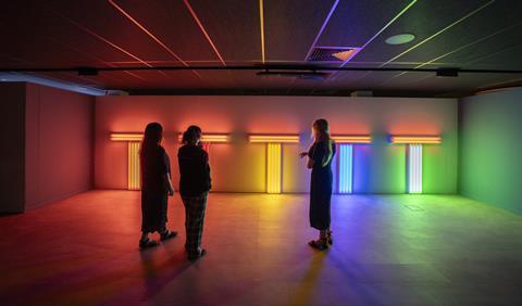 There are three people in a shadowed room, admiring light displays of many colours.