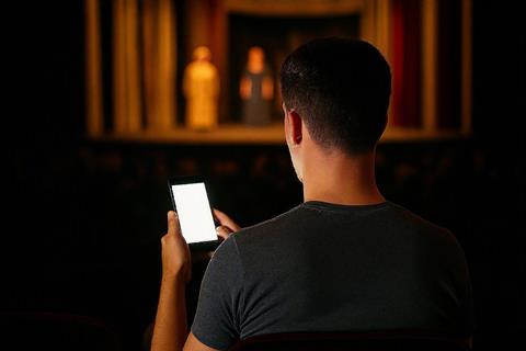 Man holding mobile phone in dark theatre