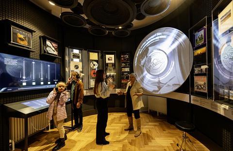 Two kids listen to an audio exhibit while two adults talk