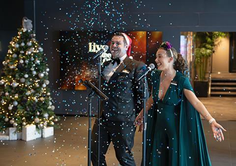 Two people singing in front of christmas tree